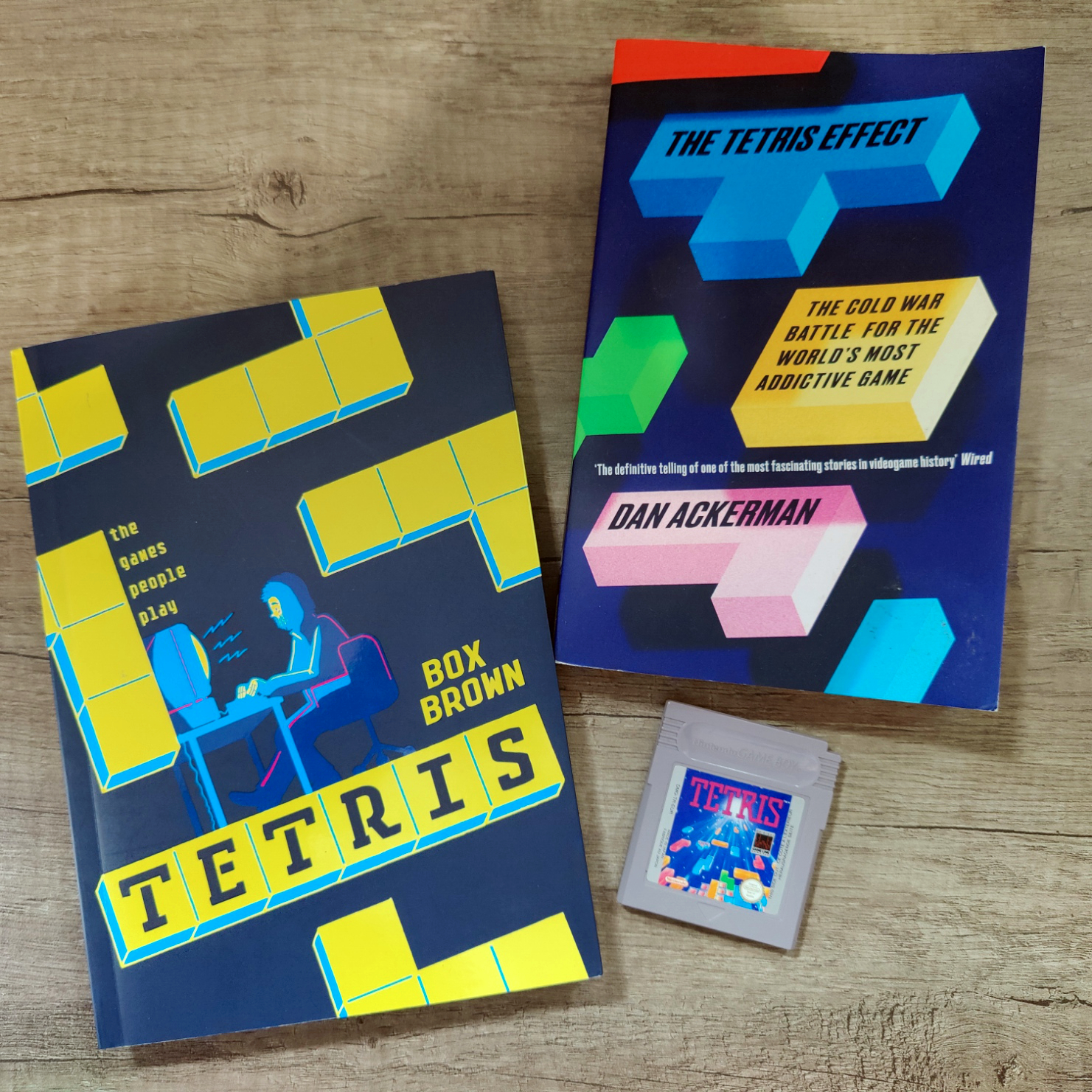 Two Books and a Tetris Gameboy Cartridge on a table - Dan Ackerman's "The Tetris Effect" and Box Brown's "Tetris: The Games People Play"